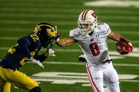 This image shows former Wisconsin Badgers Running Back Jalen Berger starting to stiff arm a Michigan Wolverines defender, while running with the ball.