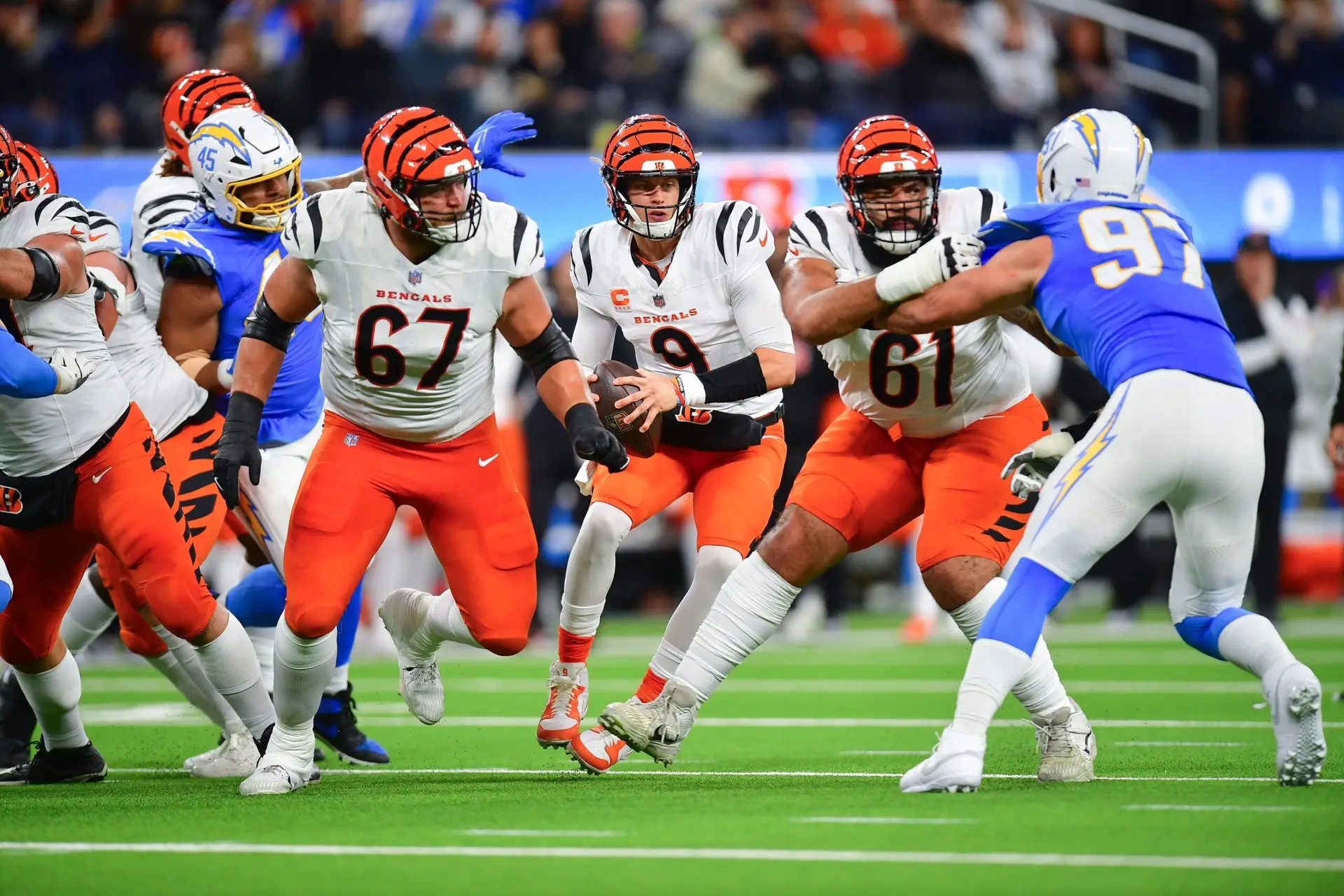 Nov 17, 2024; Inglewood, California, USA; Cincinnati Bengals quarterback Joe Burrow (9) moves out to pass as guard Cody Ford (61) and guard Cordell Volson (67) provide coverage against Los Angeles Chargers linebacker Joey Bosa (97) during the first half at SoFi Stadium. Mandatory Credit: Gary A. Vasquez-Imagn Images